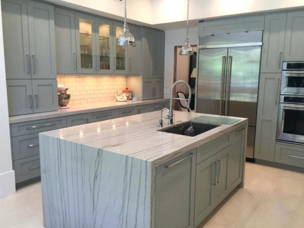 A kitchen with marble counter tops and grey cabinets.